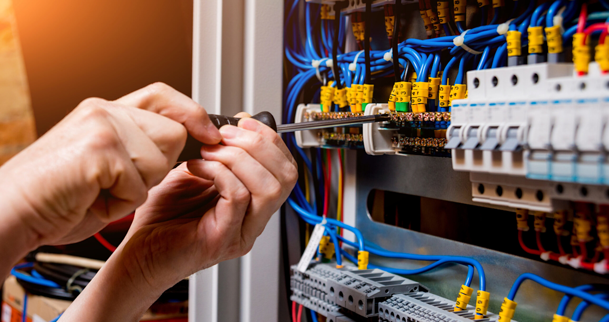 Electrician working on control panel wiring and terminal connections with blue and yellow cables